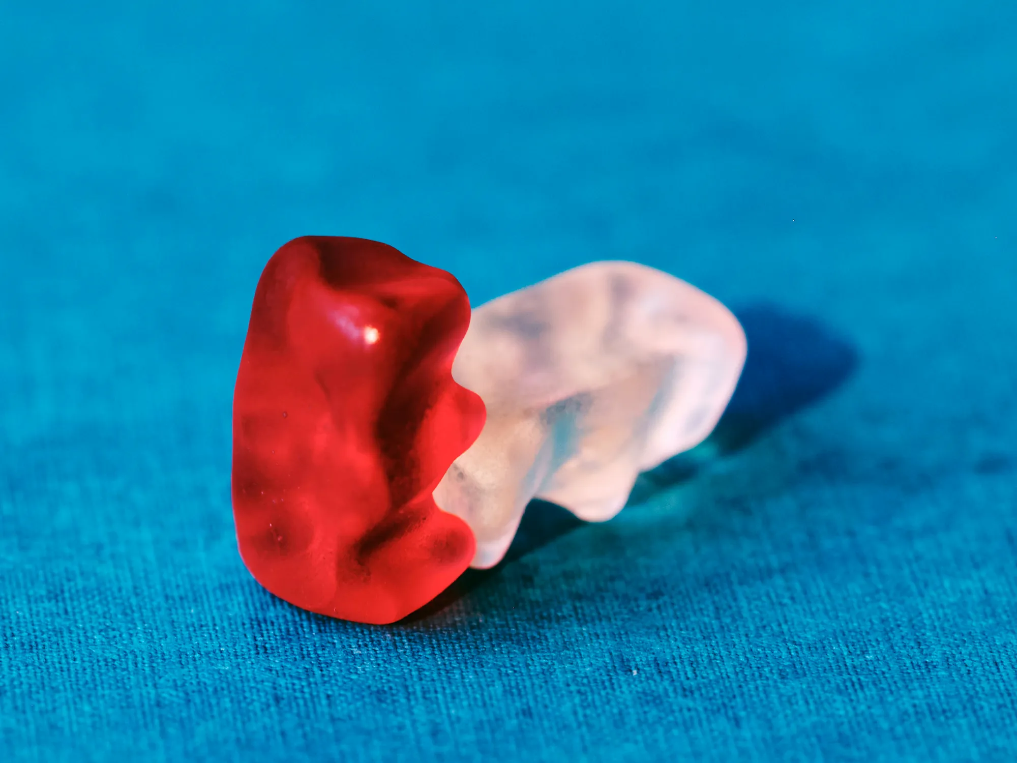Ein roter und ein durchsichtiger Gummibär auf türkisem Hintergrund