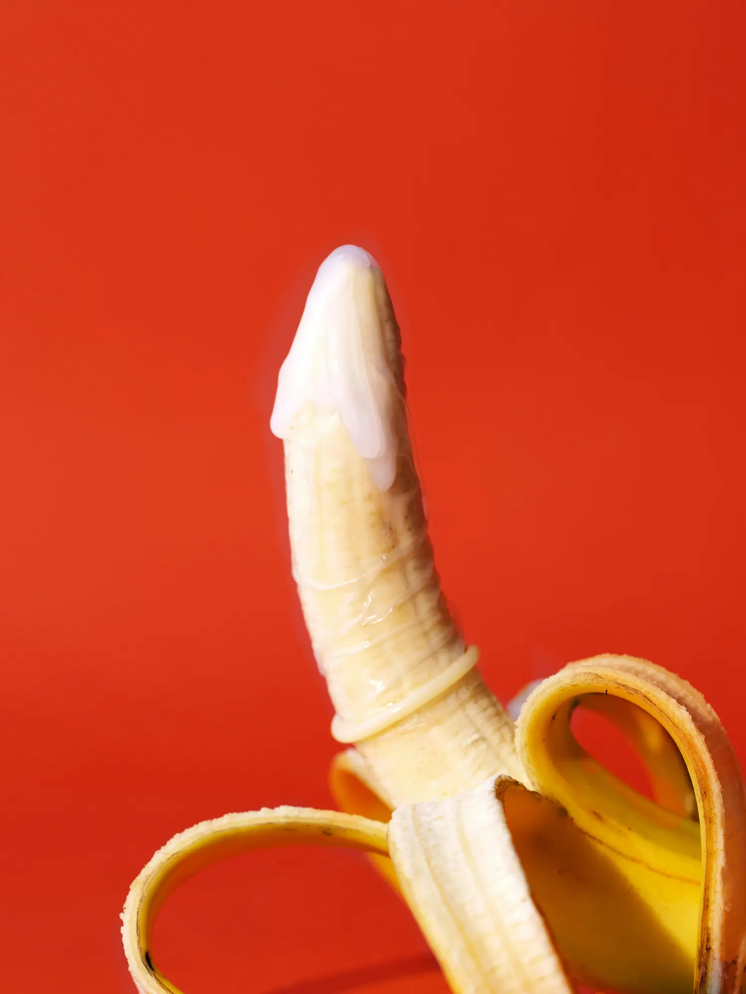 Banane mit Kondom und Creme vor rotem Hintergrund