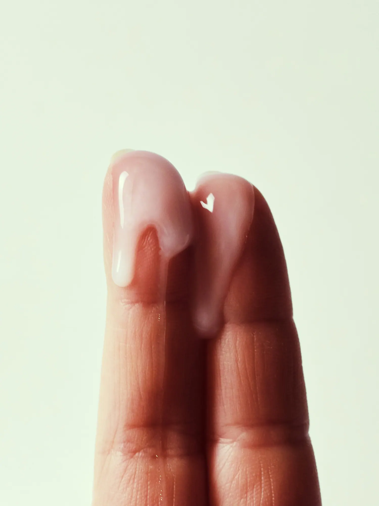 Zwei Finger mit Lotion vor hellem Hintergrund