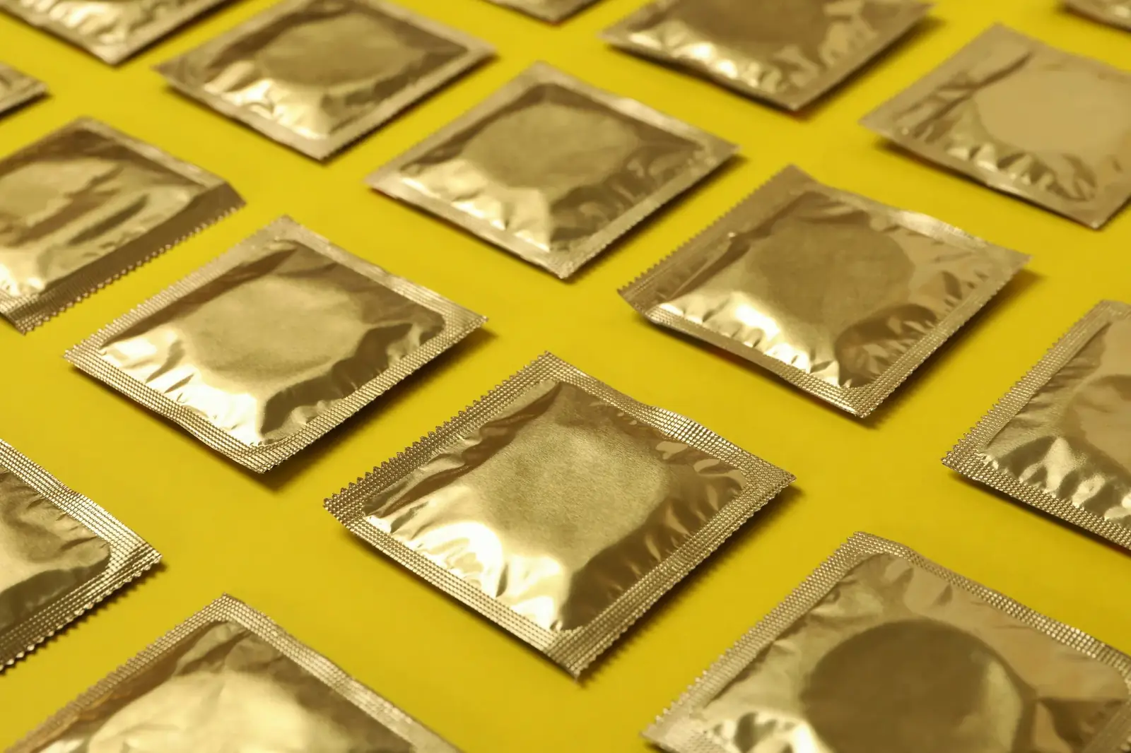 Goldene Kondompackungen in Reihen auf gelbem Grund